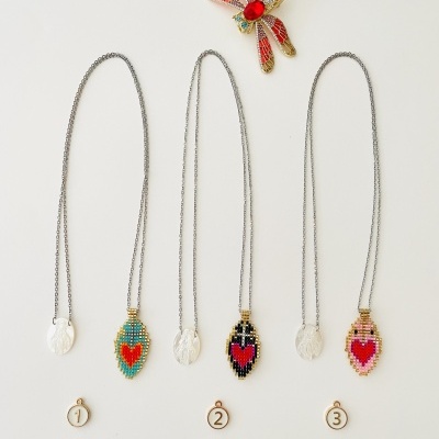 Três colares com pendentes bordados em contas com coração e um alfinete de libelinha colorida