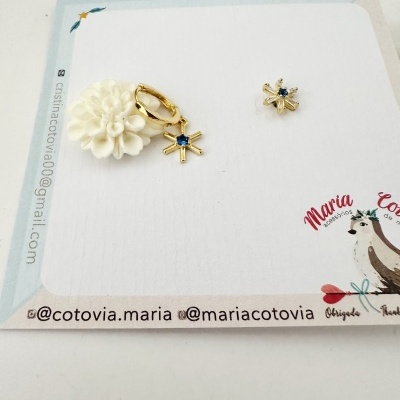 Brincos dourados em cartão com desenho de flor branca e estrela azul