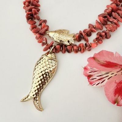Colar vermelho com detalhes dourados e peixes esculpidos ao lado de flor rosa