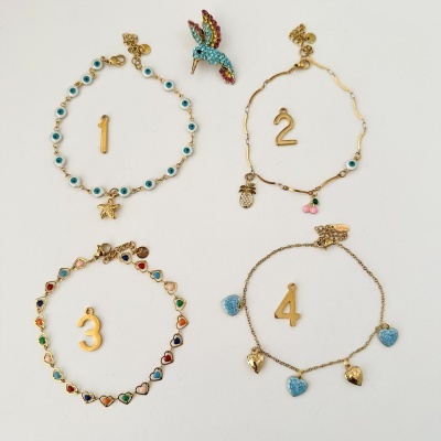 Pulseiras douradas com pendentes coloridos numeradas de 1 a 4 e broche de pássaro colorido sobre fundo branco