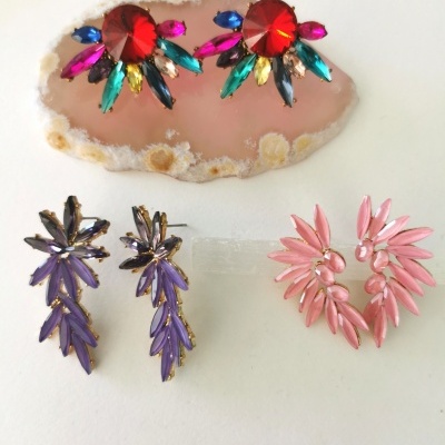 Três pares de brincos coloridos dispostos sobre uma superfície branca.