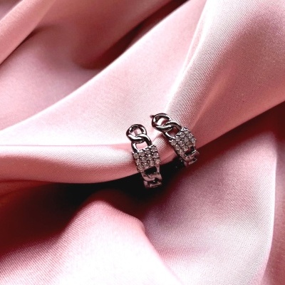 Par de argolas prateadas com pedras sobre tecido rosa.