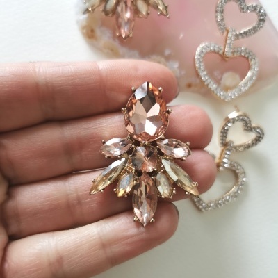 Brinco em pedras rosa e douradas facetadas, e brincos de coração com pedras brilhantes sobre fundo branco.