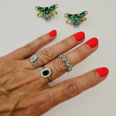 Brincos em forma de abelha e mão com unhas vermelhas e anéis coloridos