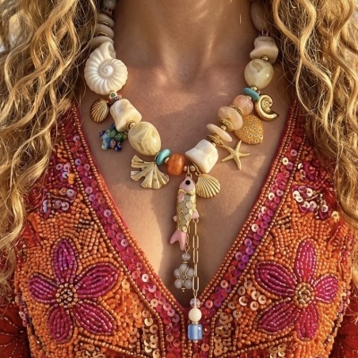 Colar colorido com pedras, conchas e pendente de peixe usado com blusa bordada floral laranja e vermelha