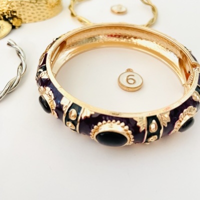 Pulseira dourada com esmalte roxo e pedras pretas junto com outros acessórios