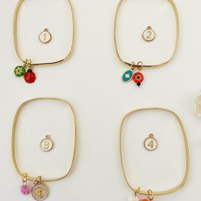 Pulseiras douradas quadradas com pendentes coloridos numerados em fundo branco