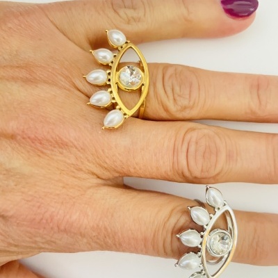 Dois anéis em forma de olho com pedras brancas, usados em dedos de mão com unhas vinho.