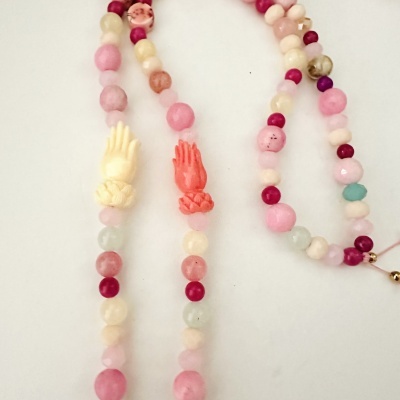 Colar com contas coloridas e duas contas em forma de mãos sobre fundo branco.