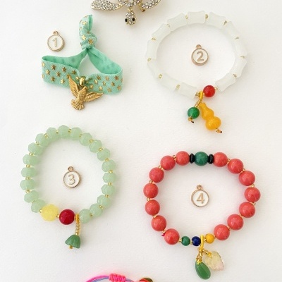 Cinco pulseiras coloridas numeradas e uma joia brilhante em forma de caranguejo em fundo branco