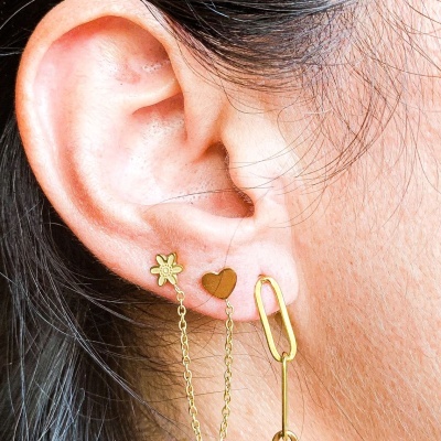 Brincos dourados com corrente e coração numa orelha