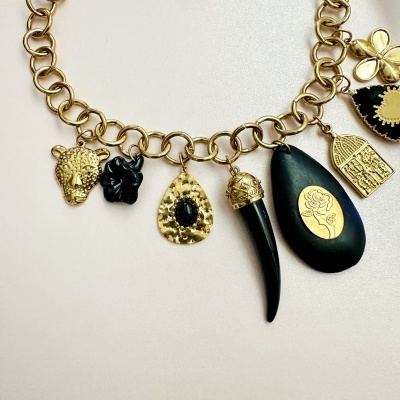 Colar dourado com pendentes variados em preto e dourado, sobre fundo claro