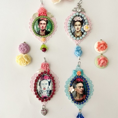 Pendentes ovais coloridos com imagens de Frida Kahlo e flores artificiais sobre fundo branco.
