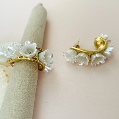 Conjunto de anel e brinco florais brancos e dourados sobre fundo rosa