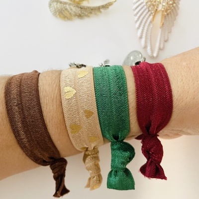 Pulseiras coloridas de tecido com nós no pulso e brincos dourados em forma de asas ao fundo