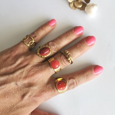 Mão com cinco anéis dourados e unhas cor de rosa