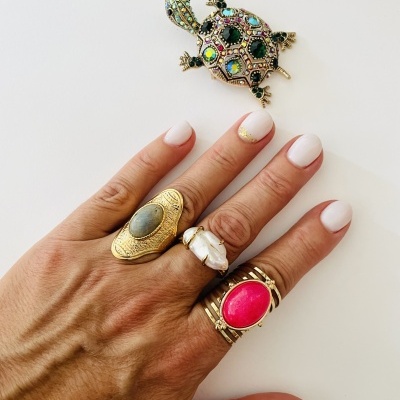 Mão com três anéis e broche de tartaruga com pedras coloridas