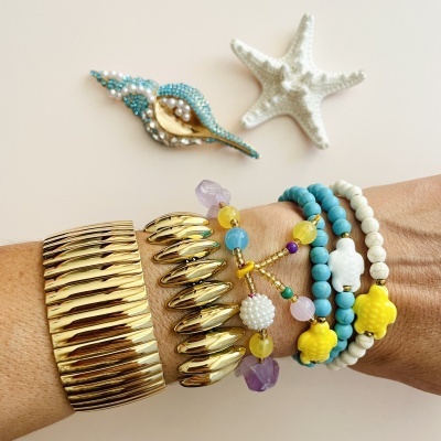 Pulso com pulseiras douradas e coloridas sobre fundo com estrela-do-mar e concha decorativa