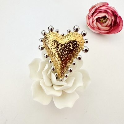 Broche em forma de coração dourado com bolinhas prateadas em cima de flor branca, flor rosa ao lado