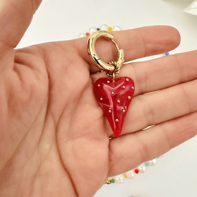 Argola dourada com pendente de coração vermelho com detalhes dourados numa mão