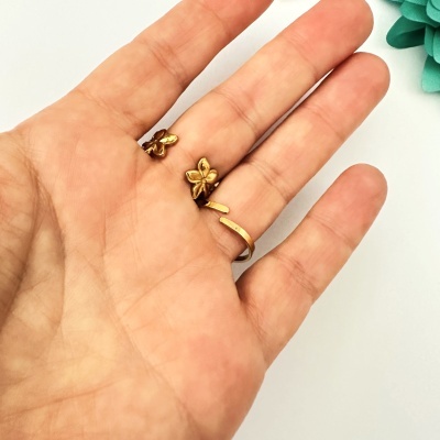 Anel dourado aberto com flores douradas na mão