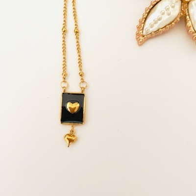 Colar dourado com pendente preto e dourado com coração, junto de broche de flor decorativa
