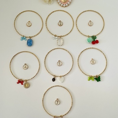 Conjunto de sete pulseiras douradas com diferentes pendentes em fundo branco e duas flores decorativas.