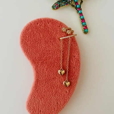 Brincos dourados com pendurado de dois corações e broche de libélula colorida sobre suporte de veludo cor de salmão