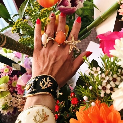 Mão com anéis e pulseiras decorativas entre flores coloridas.