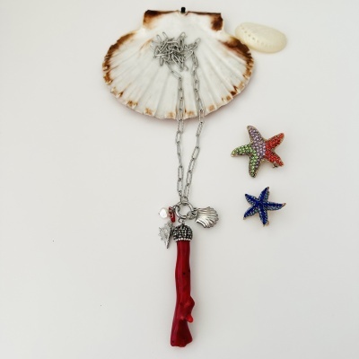 Colar com pendente coral vermelho e pingentes de conchas sobre concha natural, com broches de estrelas-do-mar coloridas ao lado.