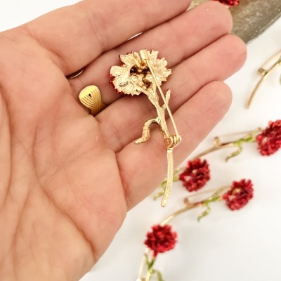 Broche flor vermelho com haste verde e base dourada na mão