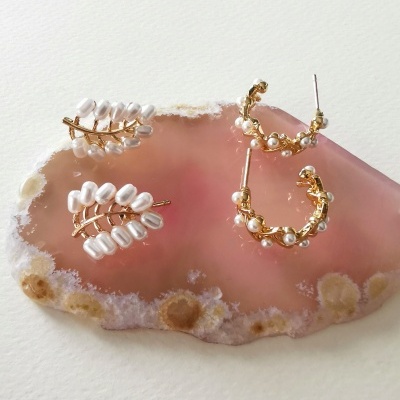 Brincos dourados com cristais e pérolas sobre pedra rosa geodadaçao