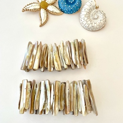 Quatro presilhas de cabelo decorativas, três pequenas em forma de flor e espirais com pérolas e uma de madrepérola em tons claros, e duas grandes feitas de madrepérola irregular, sobre fundo branco.