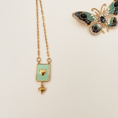 Colar dourado com pendente verde e coração dourado ao lado de broche borboleta colorido