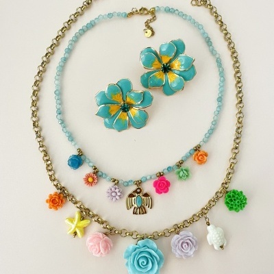 Conjunto de bijutaria colorida com flores e pendentes variados sobre fundo branco.