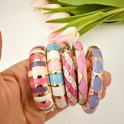 Conjunto de pulseiras coloridas em metal dourado com esmalte, seguradas por uma mão