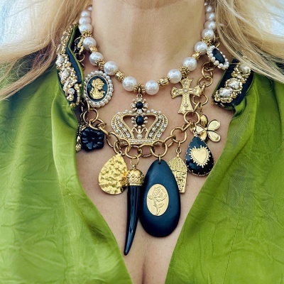 Colar decorativo com pérolas, pendentes em dourado e preto, usado sobre blusa verde.