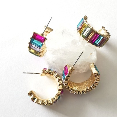 Brincos de argola dourados com pedras coloridas sobre um cristal branco