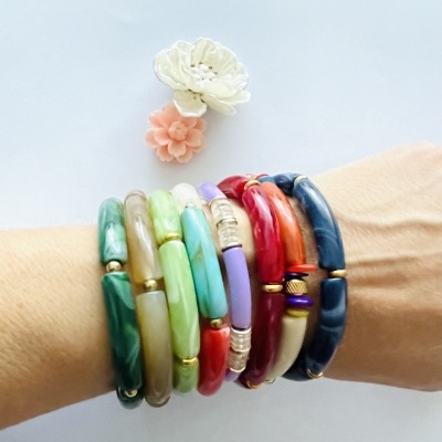 Pulseiras coloridas de resina com detalhes dourados no pulso, com duas flores decorativas ao fundo