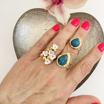 Mão com três anéis dourados com pedras e flores, prato metálico em forma de coração, flor orquídea rosa