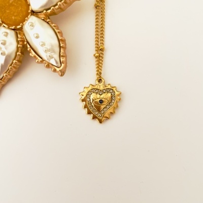Colar dourado com pendente de coração e olho azul junto a broche floral metálico