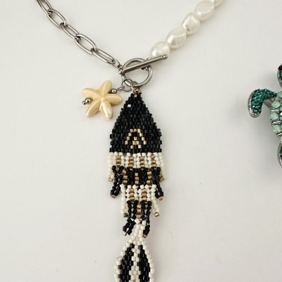 Colar com corrente metálica, pérolas brancas e pendente em forma de peixe feito de contas pretas e creme com estrela-do-mar amarelada.