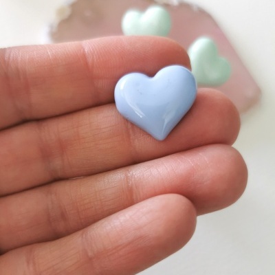 Coração azul claro brilhante segurado por dedos, com corações verdes ao fundo.