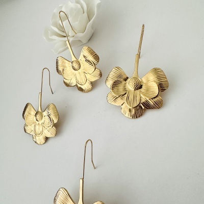 Brincos dourados em forma de flor com textura e relevos e flor artificial branca