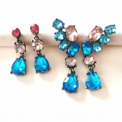 Dois pares de brincos com pedras coloridas azul turquesa, rosa e vermelho em fundo branco.
