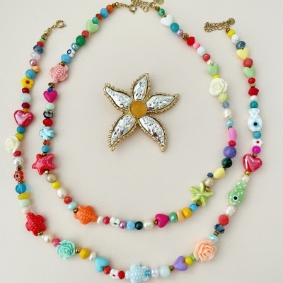 Colares coloridos com contas diversas e broche flor branco e amarelo em fundo branco