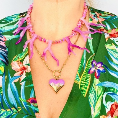 Colar com design de galhos cor-de-rosa e colar dourado com coração rosa usado com camisa floral verde.