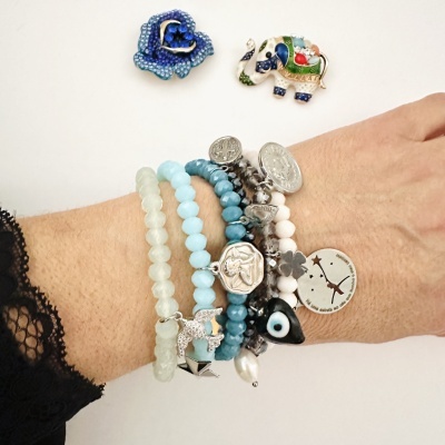 Pulseiras de contas coloridas com pingentes prateados no pulso, broches de flor azul e elefante colorido no fundo branco