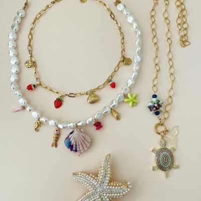 Três peças de joalharia com conchas, pérolas falsas e pendentes coloridos sobre fundo bege.