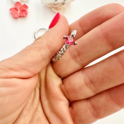Anel prateado com pedra rosa segurado por mão com unha pintada de vermelho.